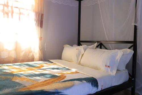 a bedroom with a bed with white pillows and a window at Duggers Motel Lusaze in Kampala