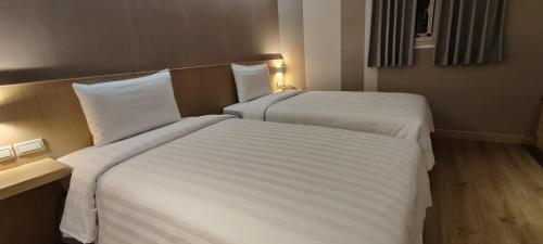 two beds in a hotel room with white sheets at Ta Lee Hotel in Tainan