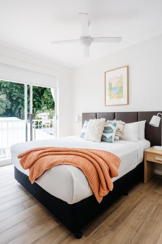 a white bedroom with a large bed with an orange blanket at Portsea 74 - Live a little in Port Douglas