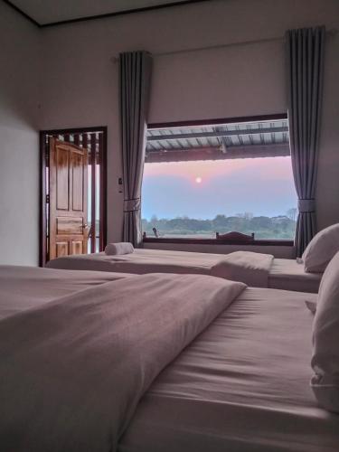 a bedroom with three beds and a large window at DODAND Studio & Sunset Riverside Guesthouse in Don Det