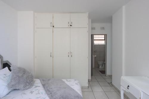 a white bedroom with white cabinets and a bed at 504 Amazibu Holiday Flat- Paradise on the Beach in Amanzimtoti