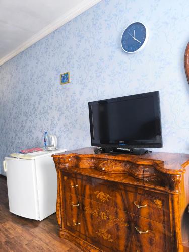 a television on top of a wooden dresser with a clock at Гостиничный комплекс Алтай in Lenīnogorsk