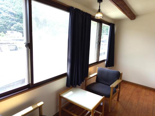 ein Raum mit einem Stuhl und einem Tisch und Fenstern in der Unterkunft 亀井荘 in Ashikita