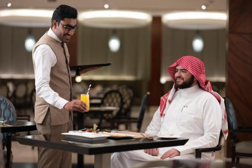 a man standing next to a man sitting at a table at Swissotel Al Maqam Makkah in Makkah