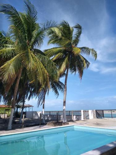 a swimming pool with two palm trees and the ocean at RS1- casa andar superior para até 8 pessoas praia do sossego itamaracá PE in Itamaracá