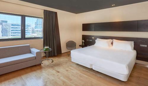 Un dormitorio con una gran cama blanca y un sofá. en NH Madrid Las Tablas, en Madrid