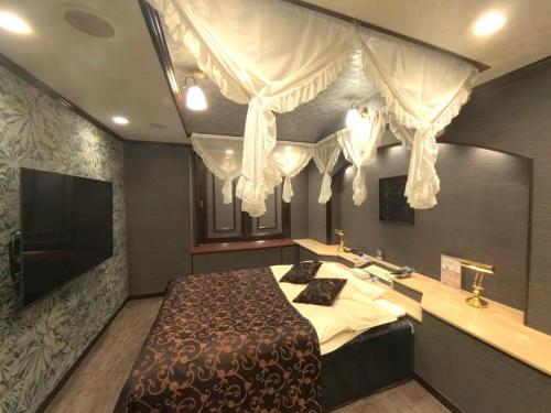 a bedroom with a bed with curtains and a television at ホテルサバナリゾートＡｄｕｌｔ Ｏｎｌｙ in Kishiwada