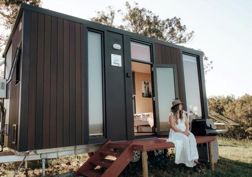 una mujer sentada en un banco frente a una casita en Amaroo One by Tiny Away, en Tuncurry