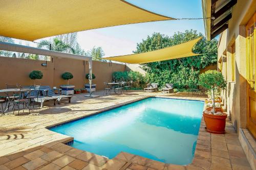 a swimming pool in a yard with a yellow umbrella at Afrique Boutique Hotel O.R. Tambo in Boksburg