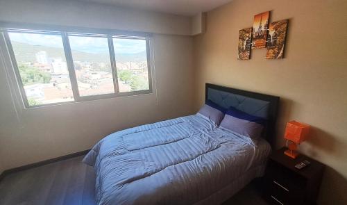 ein Schlafzimmer mit einem Bett mit blauer Bettwäsche und einem Fenster in der Unterkunft Marmor Homes in Cochabamba