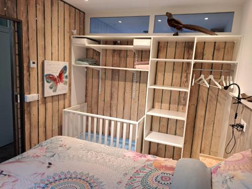 a bedroom with wooden walls and a crib with a bird on a shelf at 't Grüne Huysje in Otterlo