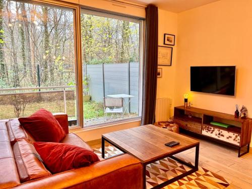 a living room with a couch and a table and a large window at Havre de paix avec jardin et parking à Chantilly in Gouvieux
