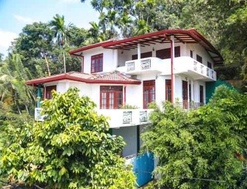 a white house with red windows and trees at Mountain Bliss Villa Peradeniya in Peradeniya