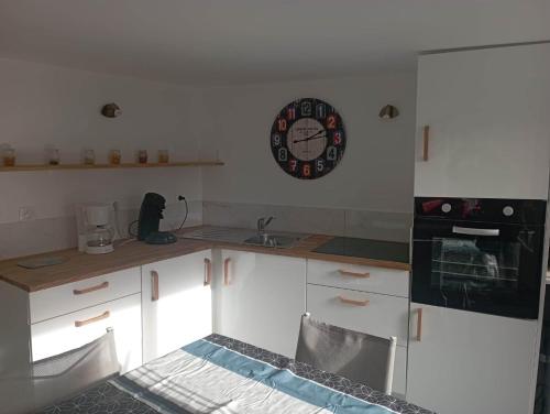 une cuisine avec des placards blancs et une horloge murale dans l'établissement Ti Louker - Appartement à 300m du Port, à Locmiquélic