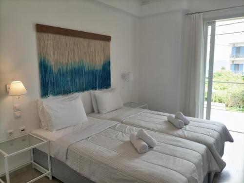 two beds in a white room with a window at Hotel Pitsakis in Tolo
