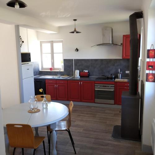 a kitchen with red cabinets and a white table with chairs at Gîte les pieds dans l'eau in Baugé-en-Anjou