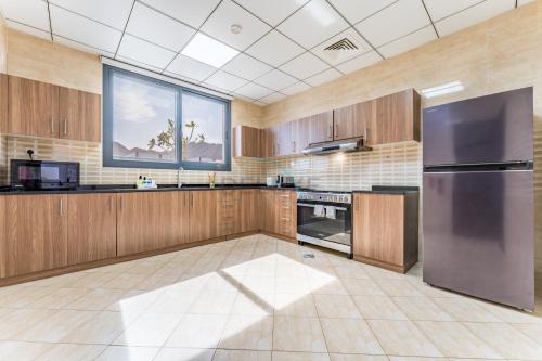 a large kitchen with wooden cabinets and a stainless steel refrigerator at Overlooking Pool & Sea Views Villa with BBQ Facility, Sharm - Al Dana Villa, Al Dana Island by Deluxe Holiday Homes in Fujairah