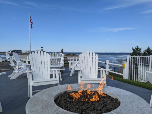 a fire pit on a patio with white chairs and the ocean at Sea Chambers in Ogunquit