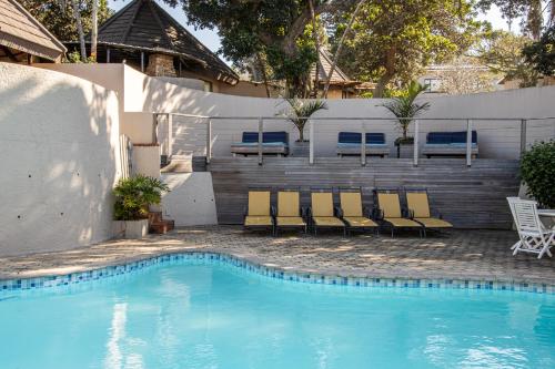a swimming pool with chairs and benches next to a fence at Tranquility - Banana Beach Club in Port Shepstone