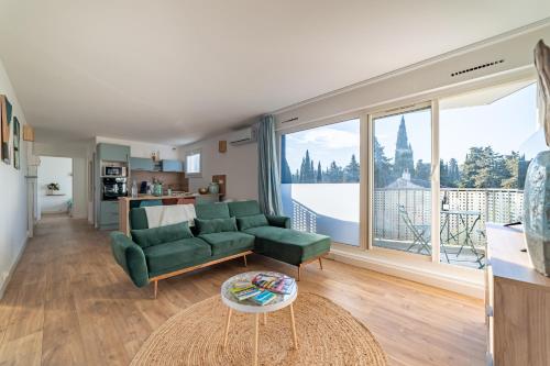 - un salon avec un canapé vert et une grande fenêtre dans l'établissement Fables du Jardin de la Fontaine, à Nîmes