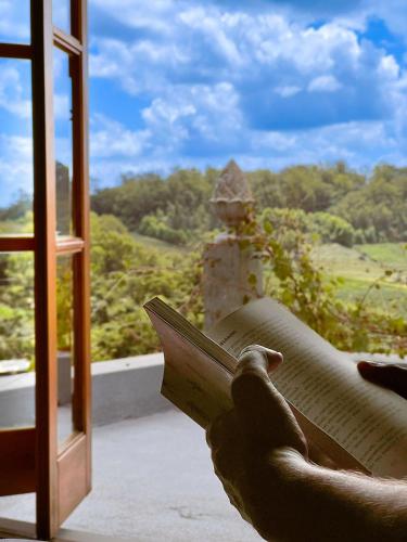 a person holding a book in front of a window at Pousada Borghetto – Charme e Exclusividade no Vale dos Vinhedos in Bento Gonçalves