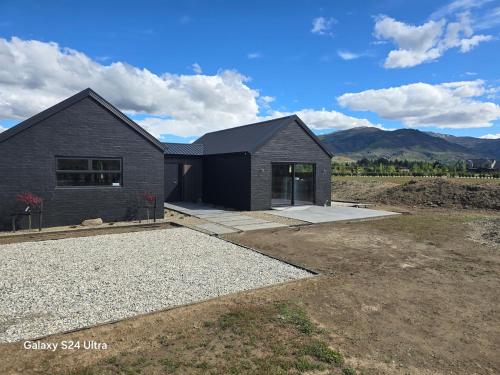 a black house in a field with mountains in the background at River Terrace Retreat Cromwell in Cromwell