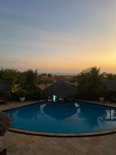 a large blue swimming pool with a sunset in the background at Pousada Aruana in Canoa Quebrada
