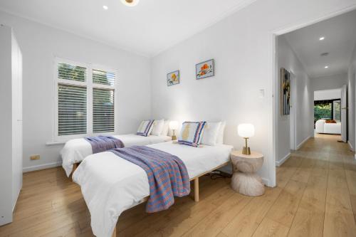 two beds in a bedroom with white walls and wooden floors at Mediterranean Muse - 3BR, Wi-Fi, Parking in Unley