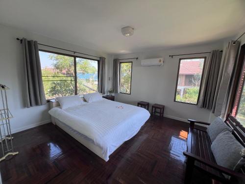 a bedroom with a white bed and two windows at Baan Plumeria บ้านภูมิเรีย in Phetchaburi
