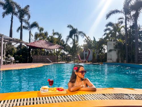 a woman sitting in a pool with a tray of food and a drink at The Neeraj River Forest Resort Ayurvedic Wellness Center in Rishīkesh