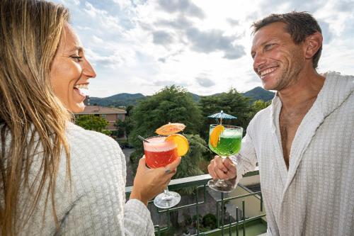 a man and a woman holding cocktails on a balcony at Hotel Terme Olympia in Montegrotto Terme