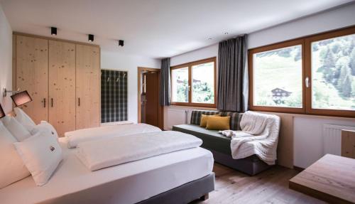 a bedroom with two beds and a chair and windows at Wanderhotel Talblick in San Giacomo