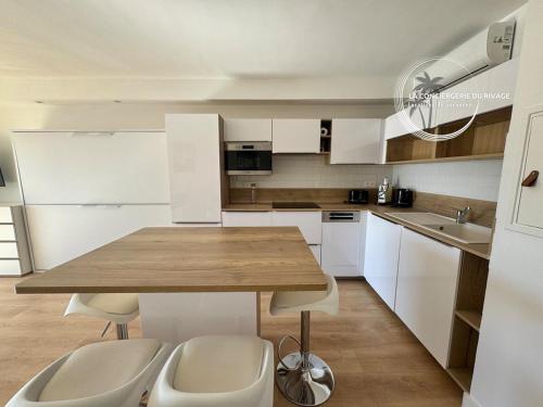 une cuisine avec une table en bois et des armoires blanches dans l'établissement Studio rénové face à la mer - Port de Carqueiranne, à Carqueiranne