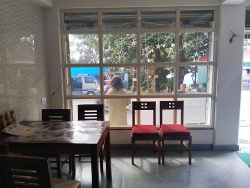a woman standing outside a window with a table and chairs at Makhamali Homestay in Karsiyang