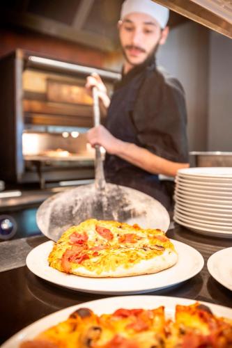 a person in a kitchen with two plates of pizza at Hôtel Club mmv Les Bergers **** in L'Alpe-d'Huez