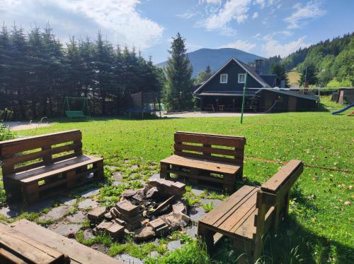 two wooden benches in a field with a house in the background at Chata Urban Filipovice in Bělá pod Pradědem