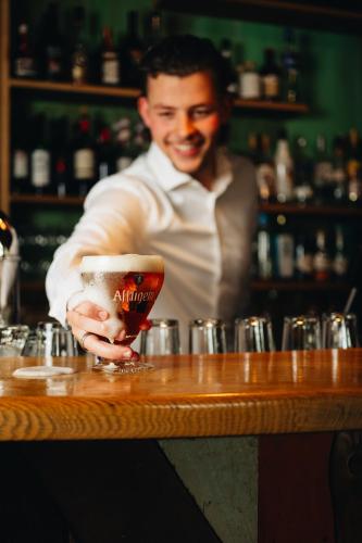 a man standing at a bar holding a drink at Hotel de Zeeuwse Stromen - Duinpark in Renesse