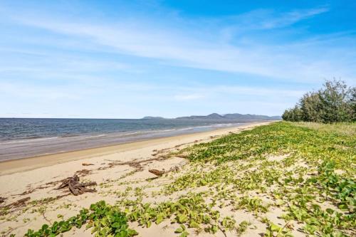a sandy beach with grass and the ocean at Ocean Spray in Sims Esplanade in Yorkeys Knob