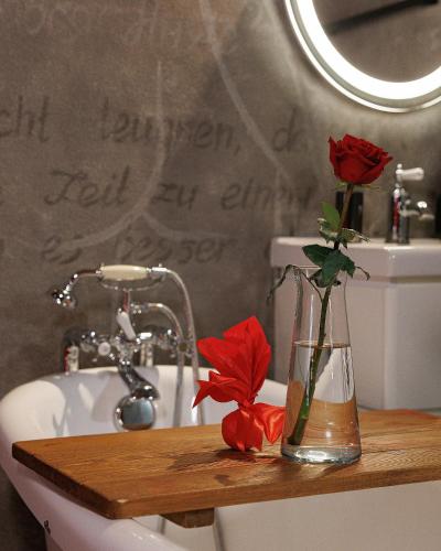a vase with red roses sitting on a bathroom sink at Masoch. Hotel & Cafe in Lviv