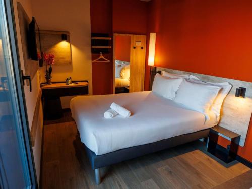 a bedroom with a large white bed with an orange wall at ibis budget Logroño Centro in Logroño