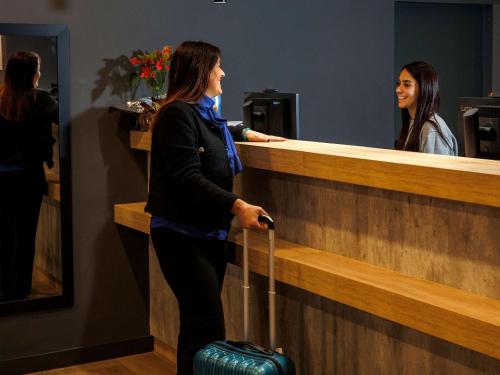 a woman standing at a counter with her luggage at ibis budget Logroño Centro in Logroño