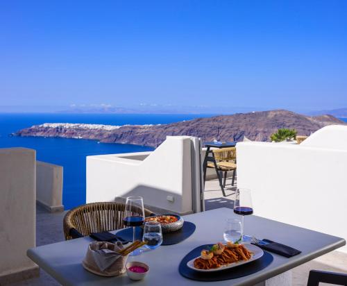 a table with food and wine glasses and a view of the ocean at Andromeda Villas & Spa Resort in Imerovigli