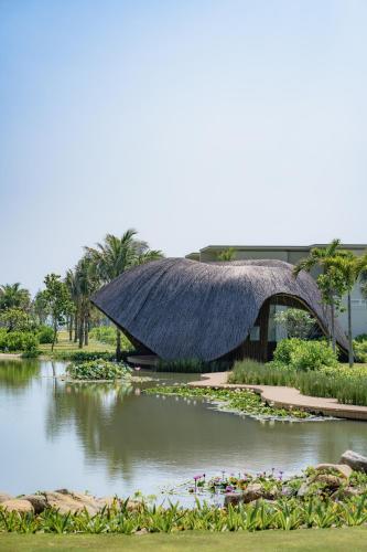 a building with a thatched roof on top of a pond at The Ocean Resort by Fusion Quy Nhon in Quy Nhon