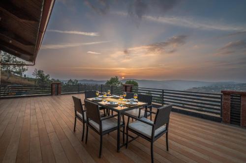 a dining table and chairs on a deck with a view at SaffronStays Whistling Thrush - 6BR luxury villa with infinity pool, gym, sauna & 13-acre estate near Table Land in Panchgani