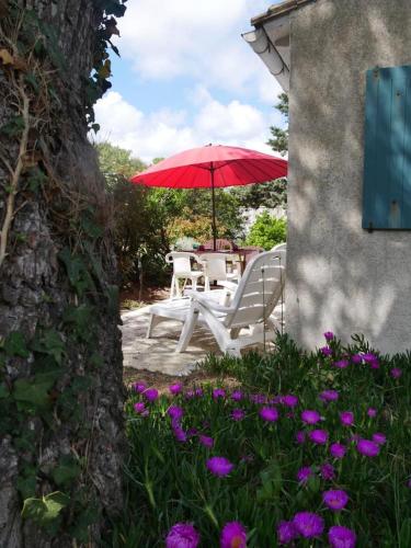 une table avec un parapluie rouge et des fleurs violettes dans l'établissement ღ La Pause Retaise - Proche Plage, Jardin & Wifi, au Bois-Plage-en-Ré