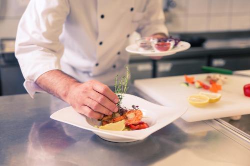 a chef holding a plate of food on a counter at Mercure Hotel Köln West in Cologne