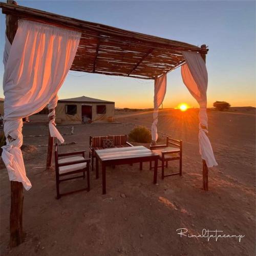 a table and chairs under a canopy with the sunset at Rimal tata camp in Migourdâne