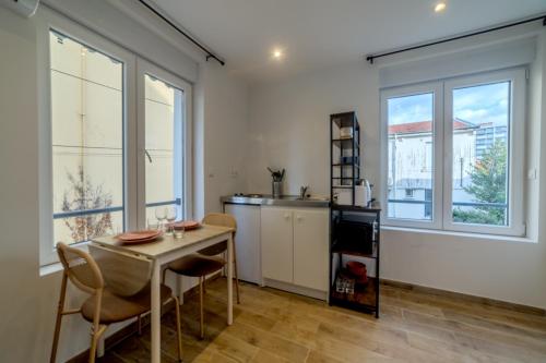 une cuisine avec une table, des chaises et des fenêtres dans l'établissement Pasteur Collection - Confort & Design - 2pers, à Villeurbanne