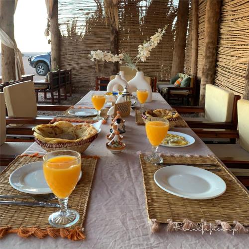 a table with plates of food and glasses of orange juice at Rimal tata camp in Migourdâne