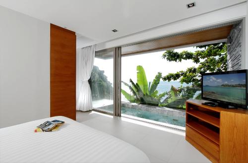 a bedroom with a television and a large window at Cape Sienna Phuket Gourmet Hotel & Villas - SHA Extra Plus in Kamala Beach